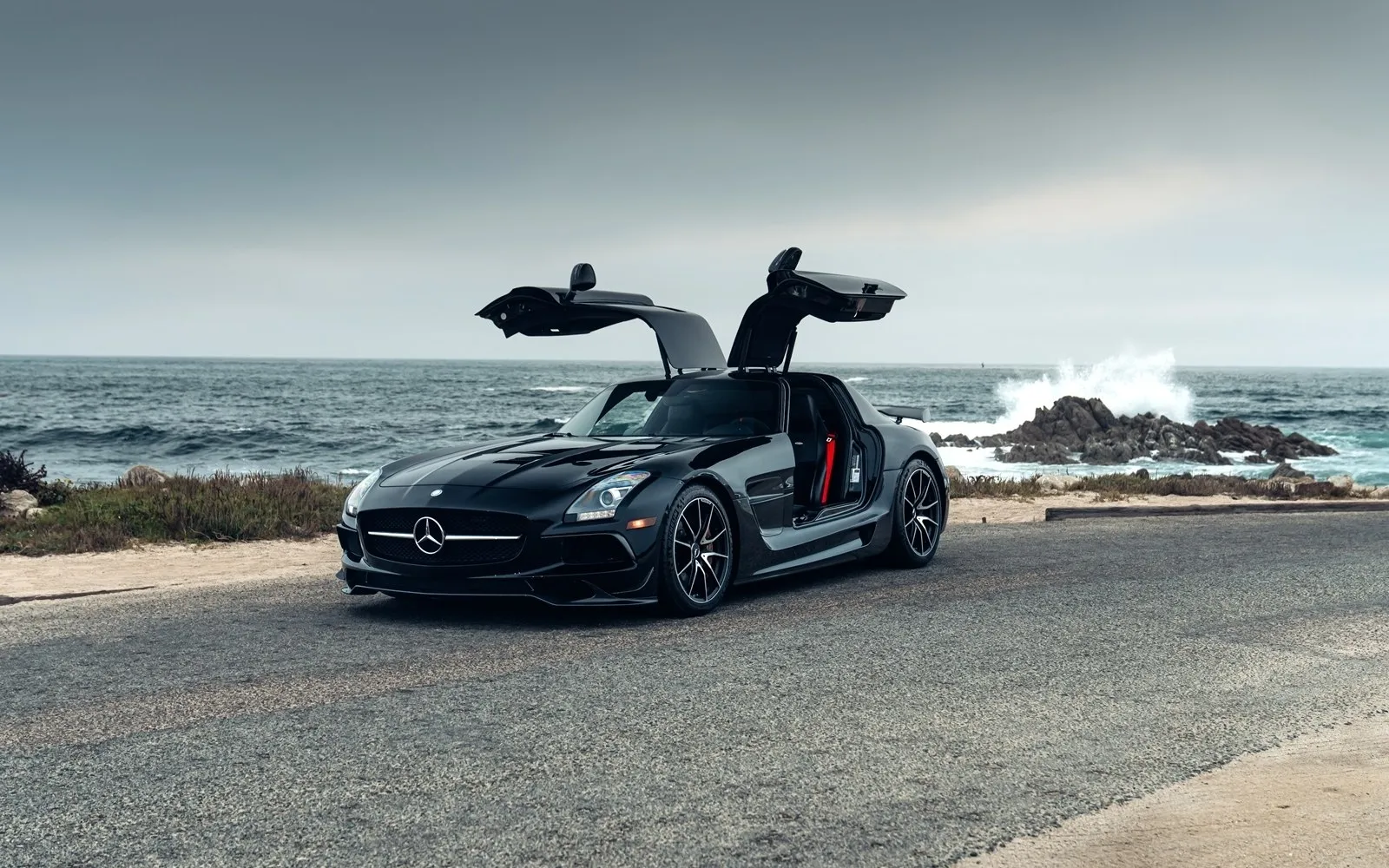 A Mercedes-Benz SLS AMG beside the sea, its gullwing doors open